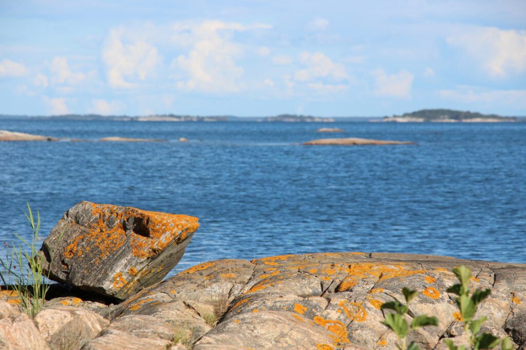 Cliffs in the archipelago of Åland with stones coverd in lichen in the front and the sea (blurred) in the back.